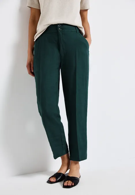 Frau trägt grüne Hose, cremefarbenes Shirt und schwarze Sandalen.